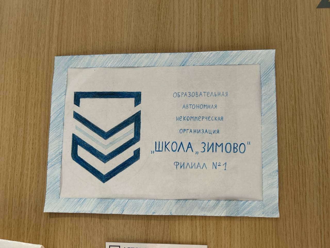 Школа Зимово Шуточная вывеска "Школа Зимово" с нарисованным синим карандашом текстом и эмблемой