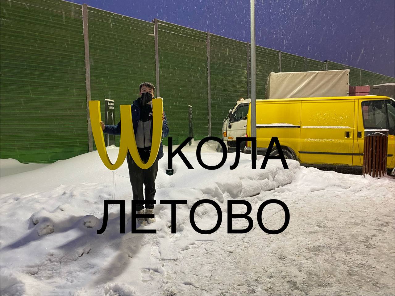 Школа Летово и буква M от McDonald’s Парень стоит на фоне сугробов с буквой «М» от McDonald’s, а на заднем плане жёлтый фургон и надпись «Школа Летово»