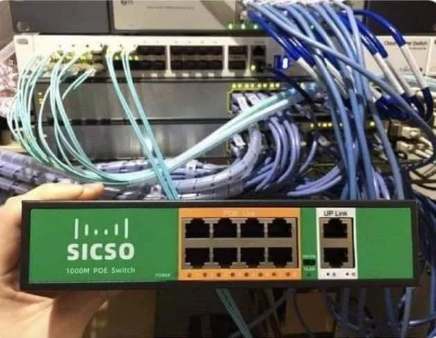 Sicso 1000M POE Switch Человек держит коммутатор Sicso 1000M POE Switch на фоне запутанных сетевых кабелей