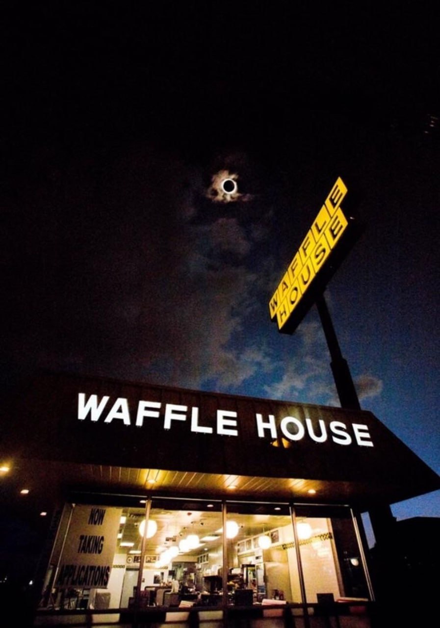Солнечное затмение над Waffle House Фотография солнечного затмения, происходящего прямо над зданием и вывеской ресторана Waffle House
