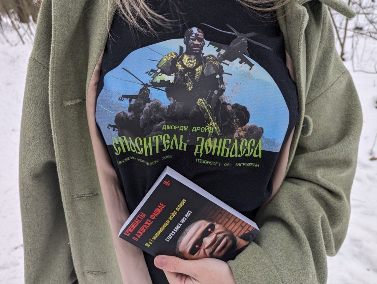 Спаситель Донбасса Девушка в зеленой куртке держит книгу «Крипипасты о Джордже Флойде» и носит футболку «Спаситель Донбасса» с изображением Джорджа Флойда в образе киборга на фоне взрывов и вертолетов.