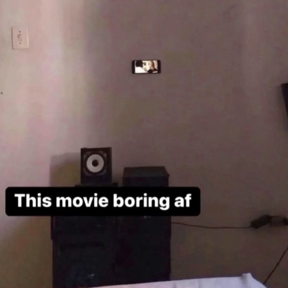 This movie boring af Мем с телефоном на стене, который показывает скучный фильм.