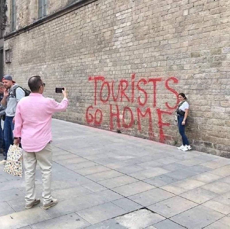 Tourists go home Барселона Мужчина фотографирует девушку на фоне надписи «Туристы, убирайтесь домой!» на стене в Барселоне.