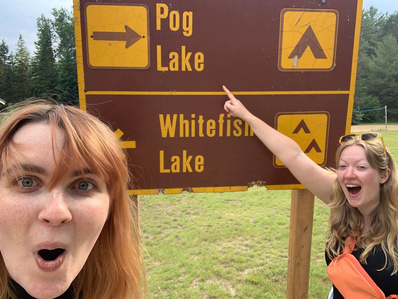 Две девушки у указателя Pog Lake Девушки с удивленным выражением лица у указателя с надписью Pog Lake и Whitefish Lake