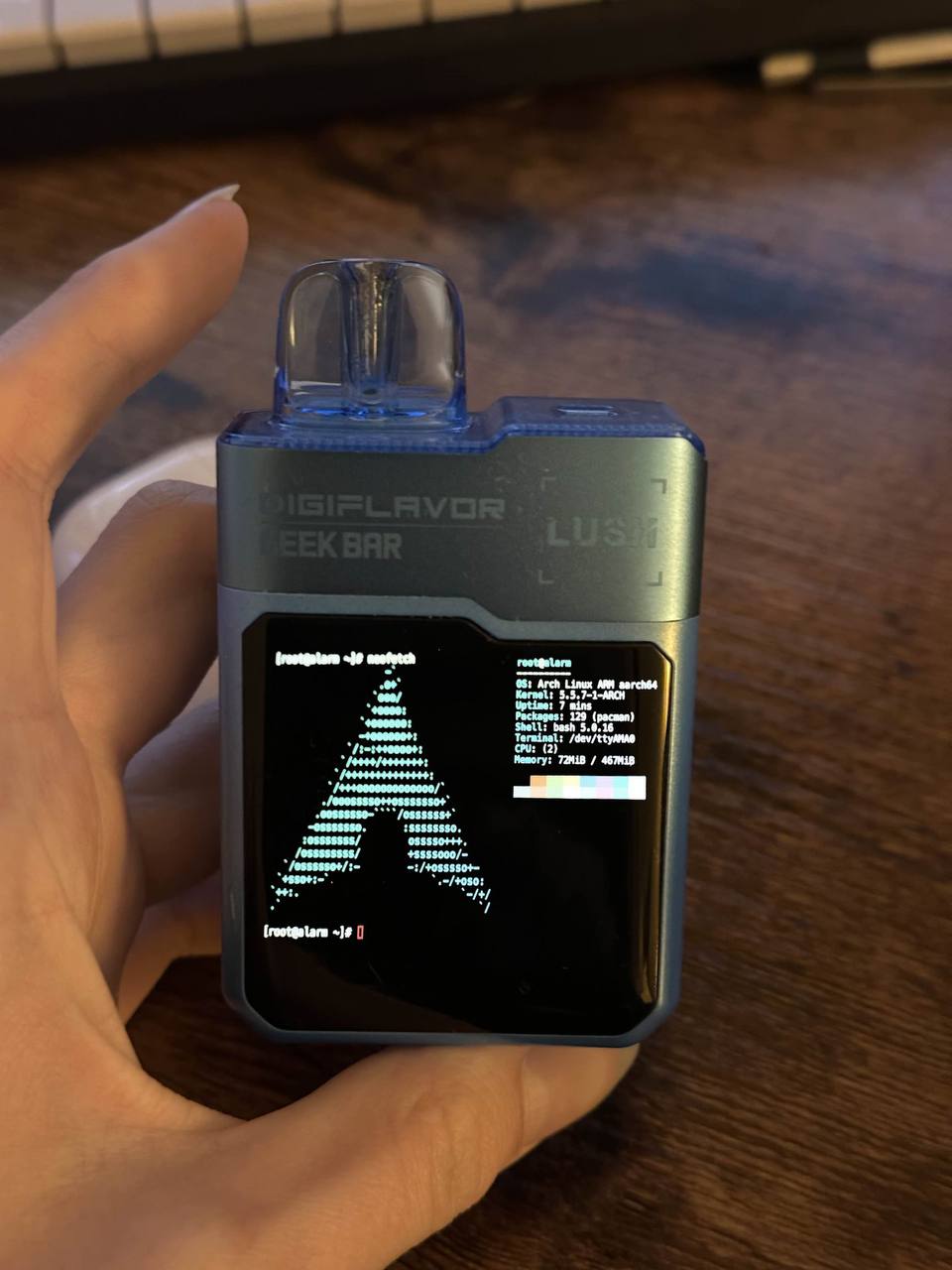 Вейп с Arch Linux Человек держит в руке электронную сигарету DIGIFLAVOR GEEK BAR LUSH с запущенной на экране Arch Linux