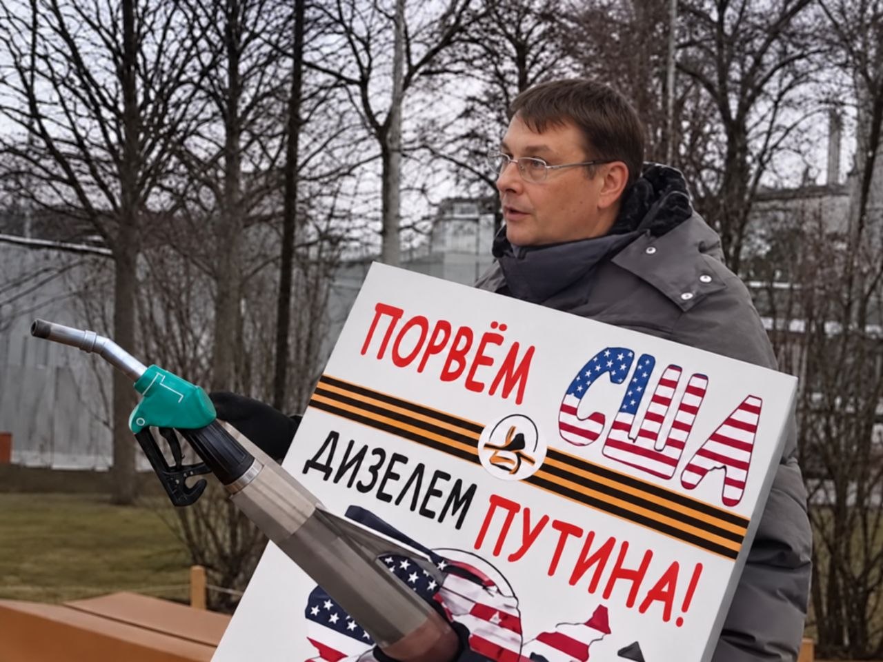 Мужчина с топливной форсункой держит плакат «Попрем США дизелем Путина!»