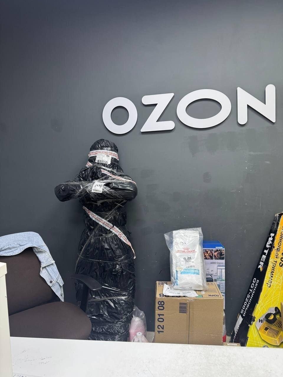 Огромная посылка в пункте выдачи Ozon выглядит как человек, замотанный в чёрный пакет и упаковочную ленту.