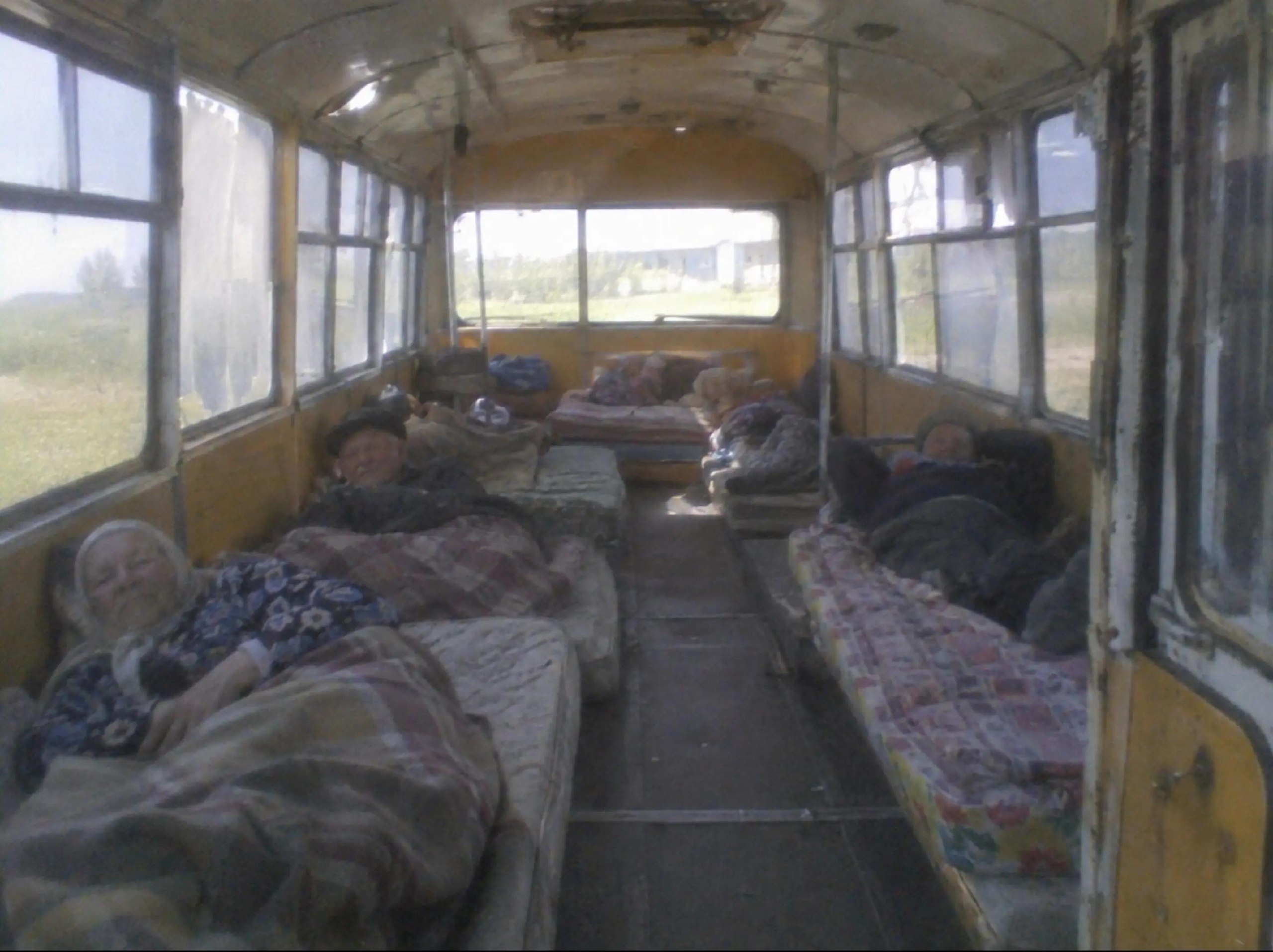Старый автобус, превращённый в общежитие: пассажиры спят на матрасах и одеялах прямо в салоне.